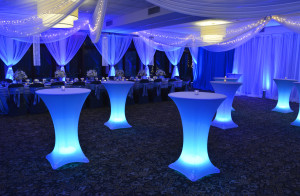 Pipe and drape used around the perimeter of room, some panels cinched to reveal windows and other used as room divider. White chiffon panels with blue uplighting.